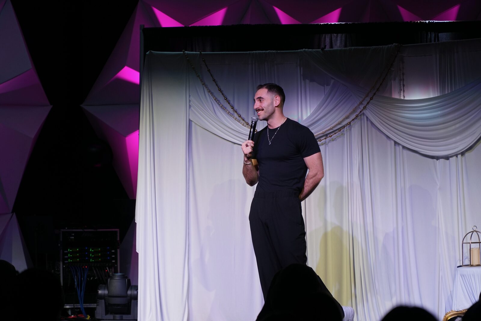 Zaid Fouzi performing at OU Arab Students Comedy Night, Norman OK, white draped backdrop with chains
