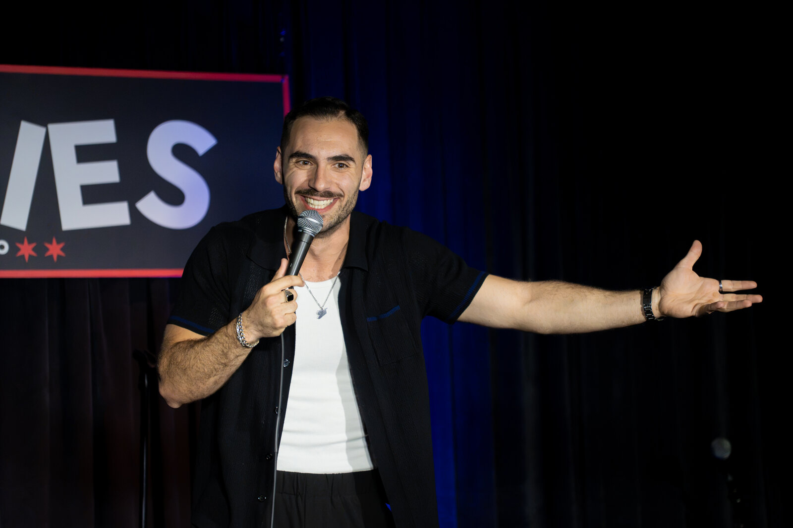 Zaid Fouzi performing on stage at Zanies Chicago, mic in hand, blue lighting