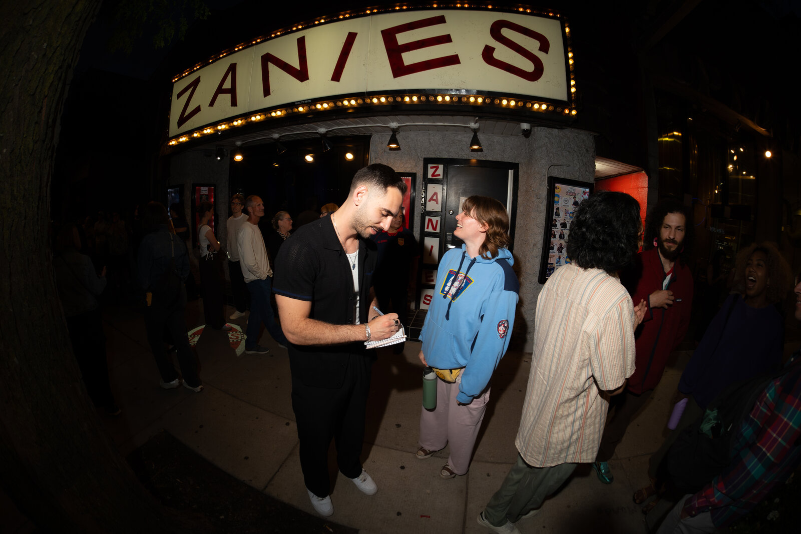 Zaid Fouzi on stage at Zanies Chicago, arms open, Zanies sign behind